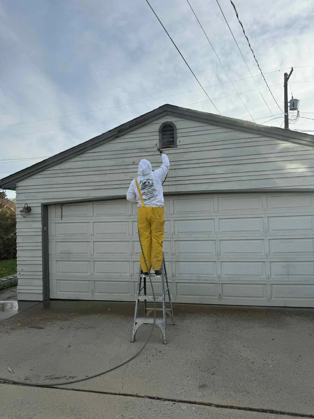 Painter on a ladder coating siding above a garage door